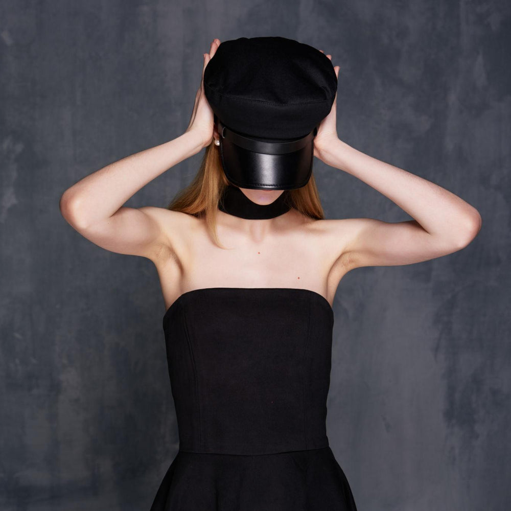 Person wearing a black dress and hat against a dark background
