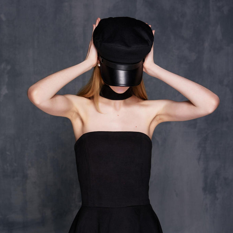 Person wearing a black dress and hat against a dark background
